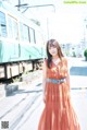 A woman in an orange dress standing in front of a train.