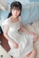 A woman in a white dress sitting on a bed.