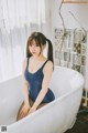 A woman in a blue bathing suit sitting in a bathtub.