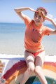 A woman in an orange shirt and red polka dot bikini sitting on a wall.