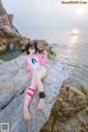 A woman in a pink and white outfit sitting on a rock by the ocean.