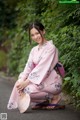 A woman in a pink kimono crouching down on the ground.