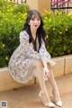 A woman sitting on a wall in a white dress.