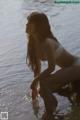 A woman in a white bikini sitting on a rock by the water.