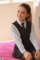 A woman in a school uniform sitting on a bed.