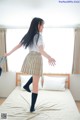 A woman in a school uniform is standing on a bed.