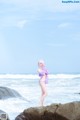 A woman in a bikini standing on a rock by the ocean.